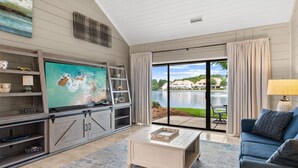A living room with a TV, wooden cabinets, a coffee table, and a view of a lake. - Lakefront Villa with 6 Seat Golf Cart (Miramar Beach)