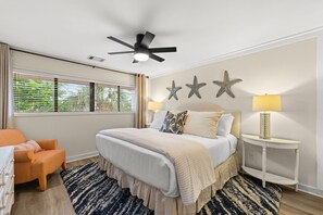 Ein Schlafzimmer mit Bett, Deckenventilator, Wanddekoration mit Sternen, Nachttisch mit Lampe und Fenster mit Jalousien.