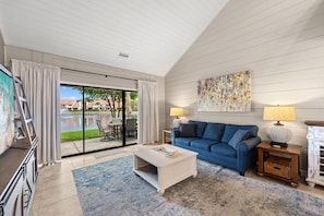 A living room with a blue sofa, a white coffee table, a lamp, and a painting on the wall. - Lakefront Villa with 6 Seat Golf Cart (Miramar Beach)