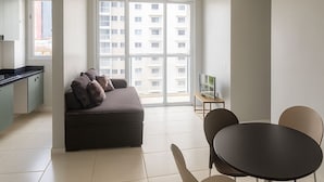 Una sala de estar moderna con sofá, una mesa de comedor con sillas, una zona de cocina y ventanas grandes.