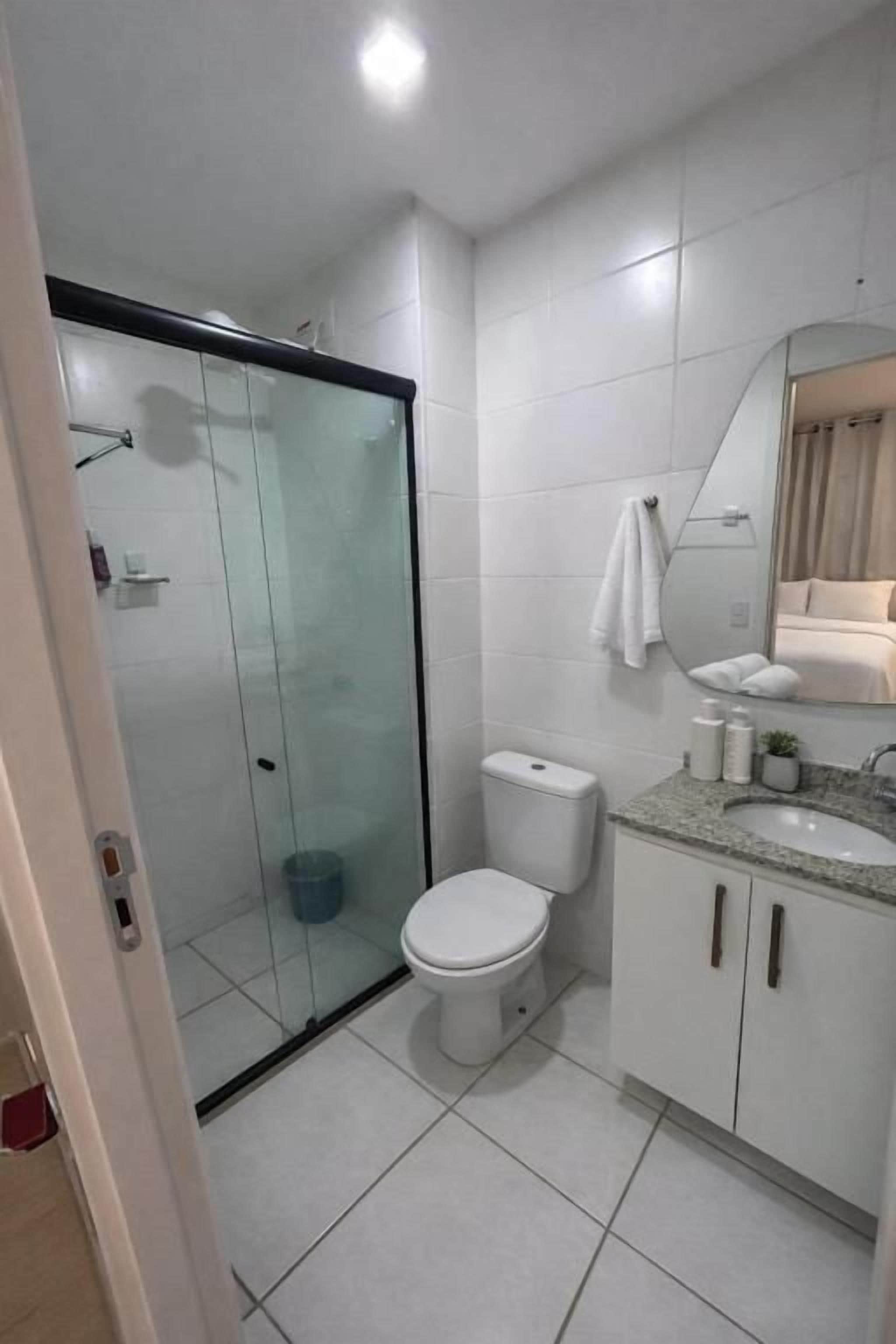 A modern bathroom with a glass-enclosed shower, a white toilet, a sink with a mirror, and a cabinet.