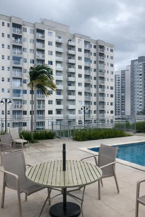 A rooftop pool area with a round table and chairs, surrounded by a high-rise building with balconies.