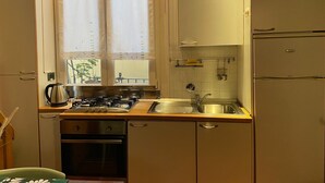 Une cuisine de taille réduite équipée d’une cuisinière à gaz, d’un four, d’un évier et d’une fenêtre avec des rideaux.