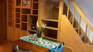 Une table à manger en bois, avec des chaises, une plante en pot et un escalier avec des rampes en bois.