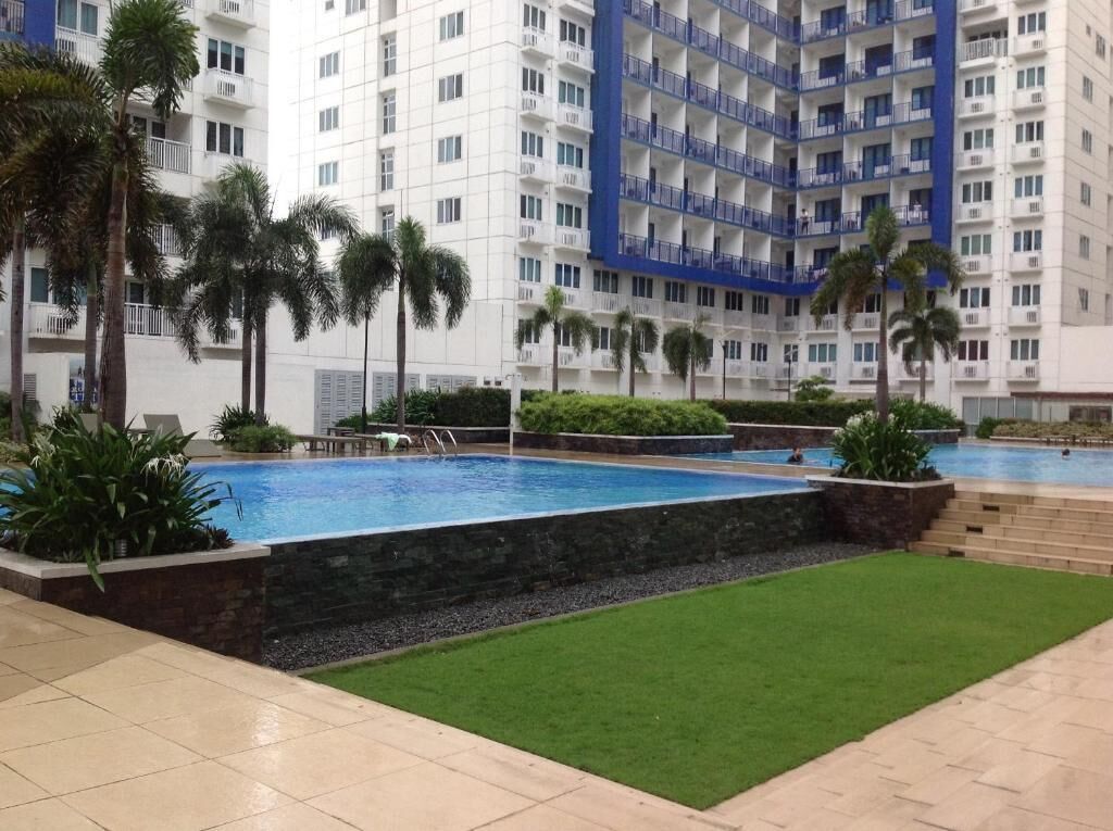 A swimming pool surrounded by palm trees and a multi-story building with balconies.