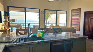 A kitchen with a large island, a dining area with chairs, and a view of the ocean.