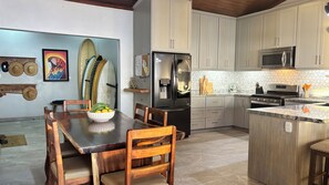 Una cocina moderna con una isla central, una mesa de comedor con sillas y tablas de surf en la pared.