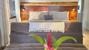 Un dormitorio con cama, mesita de noche, sofá y una planta en maceta.