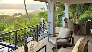 A balcony with a view of the ocean and greenery, furnished with chairs and a table. - 3BR Oceanview Haven (Dominical)