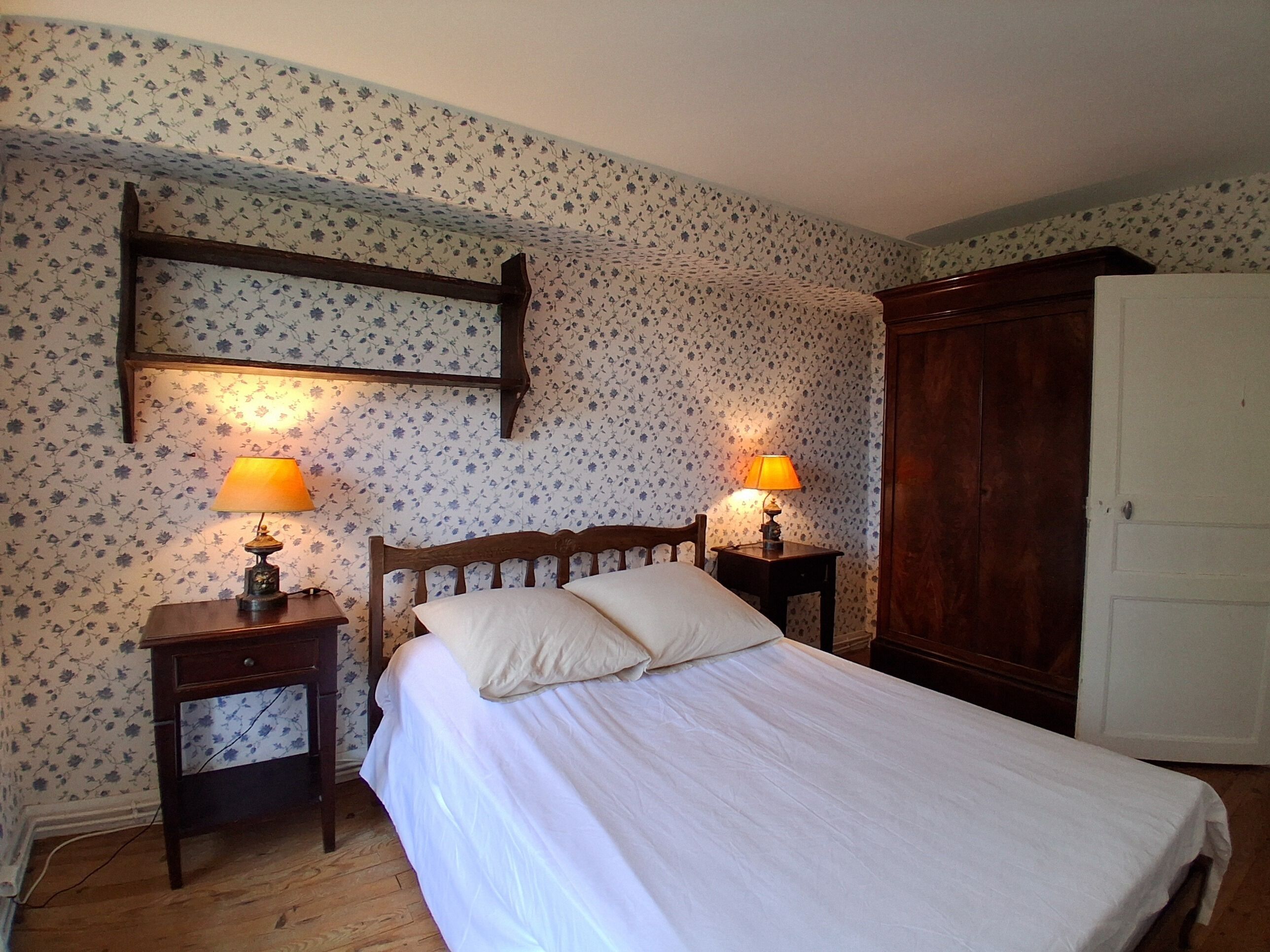 A bedroom with a wooden bed, two bedside tables with lamps, a wardrobe, and floral wallpaper.