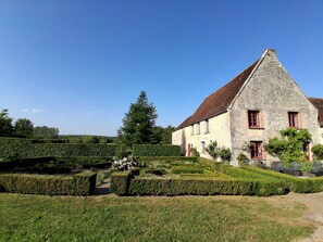 A stone building with a steep roof, surrounded by well-maintained hedges and a garden. - La Petite Cornière (Macé)