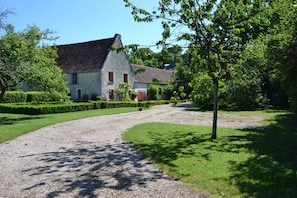Une maison de campagne avec une allée en gravier, entourée de haies et d’arbres bien entretenus.