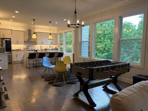 A modern kitchen with a foosball table, bar stools, and large windows. - Game Room Luxury Home @ Battery Chef Kitchen Deck (Marietta)
