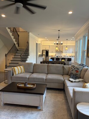 A living room with a sectional sofa, a coffee table, and a staircase. - Game Room Luxury Home @ Battery Chef Kitchen Deck (Marietta)