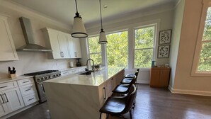 A kitchen with a large island, white cabinets, a stove, and a window with a view of trees. - Game Room Luxury Home @ Battery Chef Kitchen Deck (Marietta)