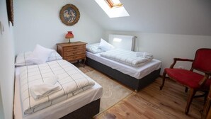 A bedroom with two beds, a wooden dresser, a red chair, a radiator, and a skylight. - Room-pension -villa Vintage Room B 105 (Tomášikovo)