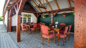 An outdoor dining area with wooden tables and chairs, a green wall, and hanging flower baskets. - Room-pension -villa Vintage Room B 105 (Tomášikovo)