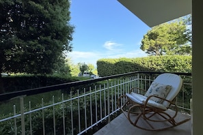 A balcony with a white rocking chair, a metal railing, and a view of a hedge and trees. - S306 - Sirolo, two-bedroom apartment with parking space (Sirolo)