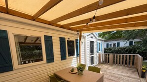 Eine überdachte Terrasse mit Tisch und Stühlen, ein Holzboden und Blick auf benachbarte Häuser.