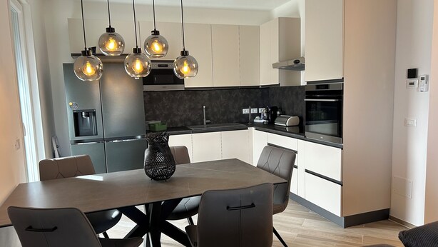 A modern kitchen with a dining area, featuring a central island, pendant lights, and built-in appliances.