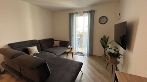 A living room with a sectional sofa, a small table, a TV, and a window with curtains.