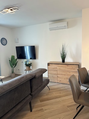 A modern living room with a flat-screen TV, a sofa, a dining area with chairs, a wooden cabinet, and a potted plant. - New 3-room apartment Lake view, pool, Lake Garda Peschiera ideal for families, couples, (Boschetti)