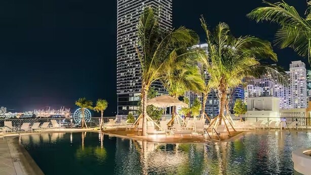 Ein nächtlicher Blick auf einen Hotelpoolbereich mit Palmen, einem Riesenrad und Hochhäusern im Hintergrund.