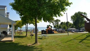 A grassy area with playground equipment, picnic tables, and a view of the sea.