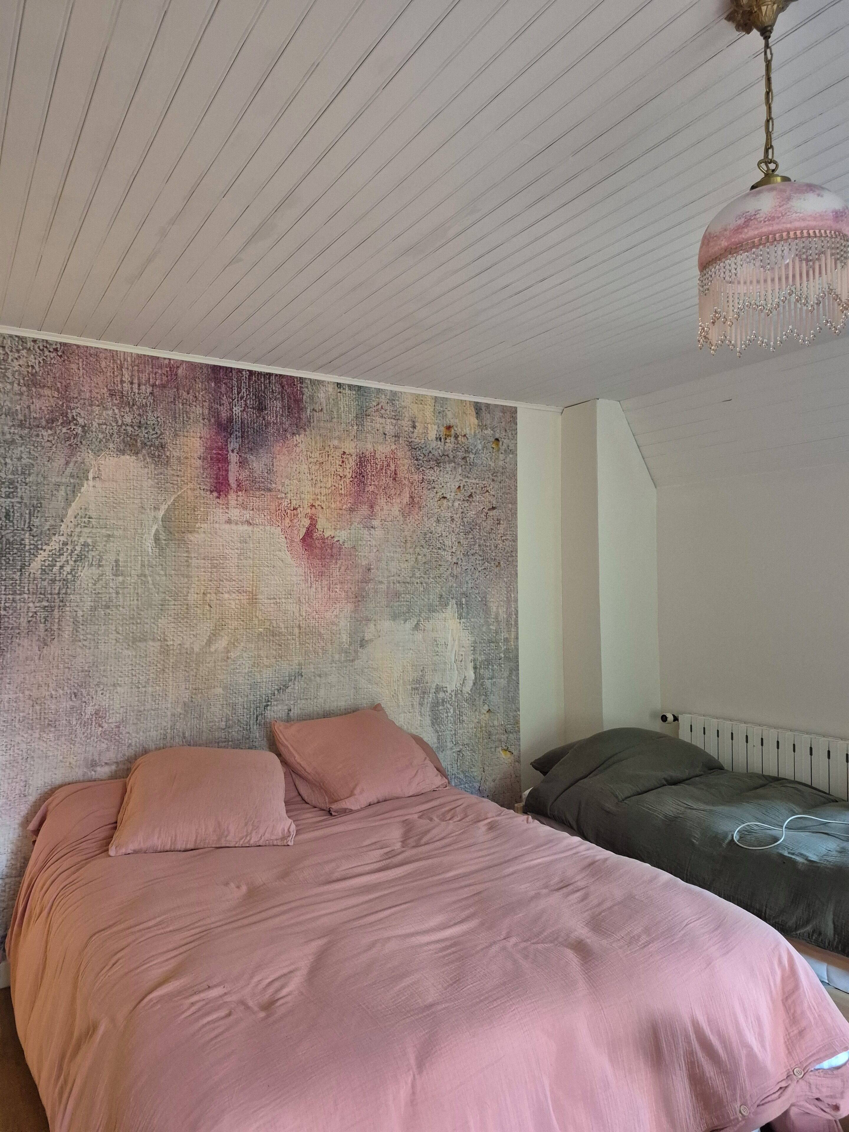 Une chambre à coucher avec un lit, une tête de lit, un radiateur et un plafond muni d’un luminaire.