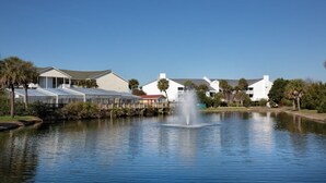 A tranquil pond with a fountain, surrounded by white buildings and palm trees. - BLOCK CW Ocean Ridge 1br (Edisto Island)