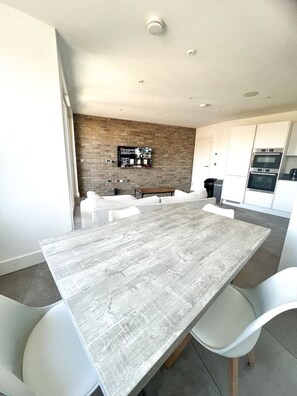 Eine moderne Küche mit weißen Schränken, einem eingebauten Backofen und einem Essbereich mit einem Holztisch und weißen Stühlen.