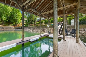 A wooden deck with a pool, outdoor seating, and a covered area.
