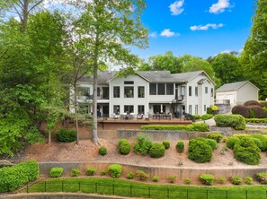 A two-story house with a deck, surrounded by well-maintained landscaping and trees.