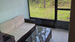 A room with a sofa and a glass-top table, large windows with a view of trees and grass. - New St. Augustine Getaway Near Beaches, Golf & Downtown Adventures (St. Augustine)
