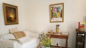 Ein Wohnzimmer mit einem weißen Sofa, einem Holztisch mit Blumenvase, einem gerahmten Gemälde und einer kleinen Kommode.