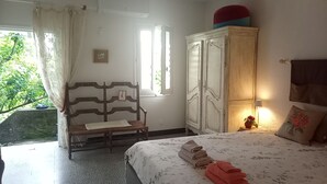 Ein Schlafzimmer mit Bett, einem Holzschrank, einer Bank, einem Fenster mit Vorhängen und einem kleinen Tisch mit Lampe.
