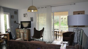 Ett vardagsrum med en soffa, en tv, en lampa och en matplats med stolar och ett bord.