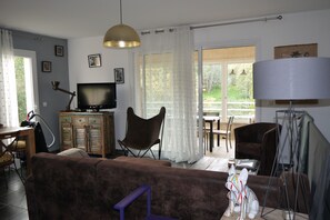Ein Wohnzimmer mit einer Couch, einem Fernseher, einer Lampe und einem Essbereich mit Stühlen und einem Tisch.