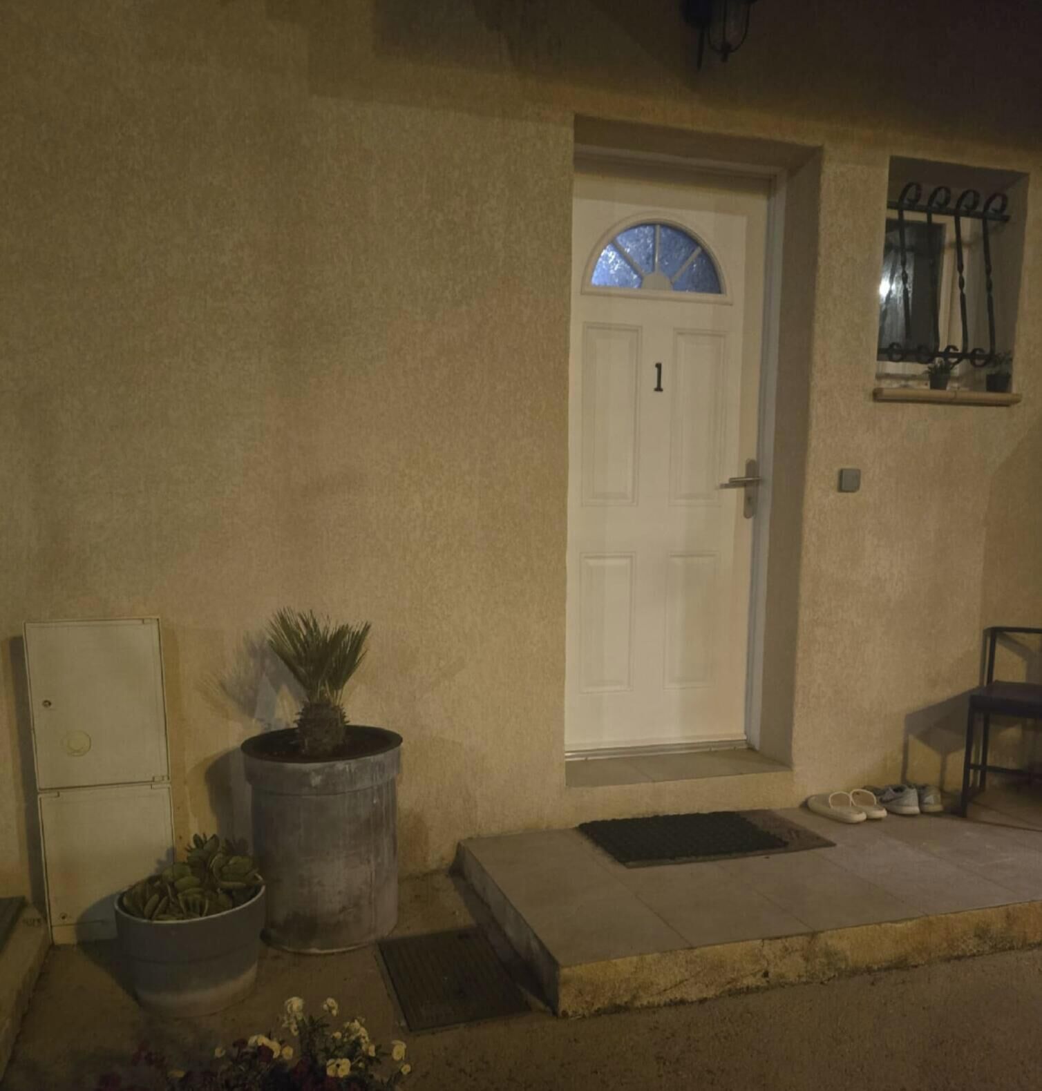 A house with a white door marked with the number 1, a potted plant, a small step leading to the door, and a chair outside.