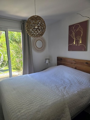 Ein Schlafzimmer mit einem großen Bett, einer hängenden Lampenschirm aus Rattan, einem wandmontierten runden Spiegel und einem gerahmten Kunstwerk.