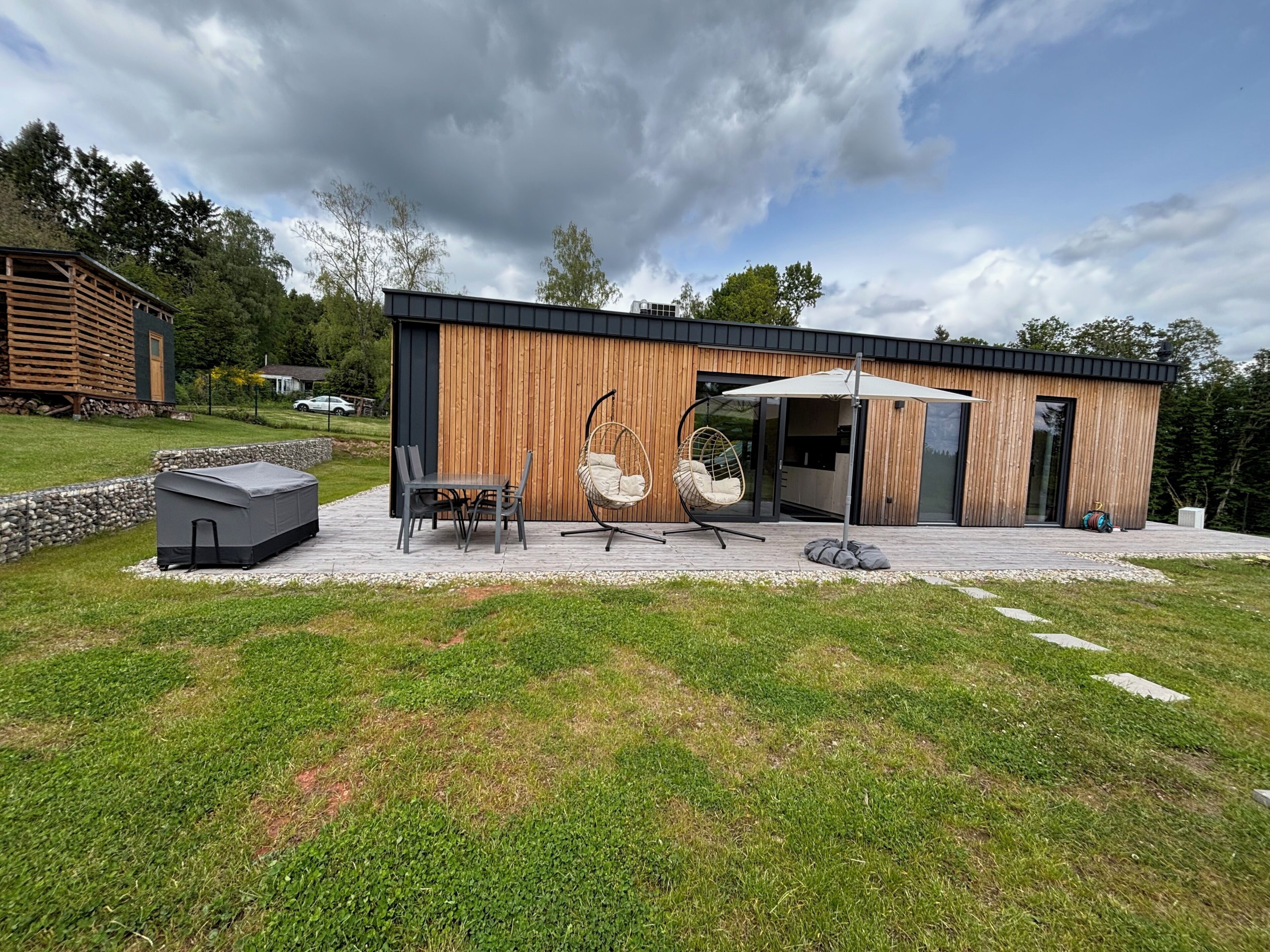 A modern building with a wooden exterior, a covered patio with a table and chairs, and a hanging chair.