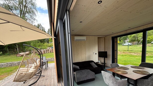 A modern living space with a wooden deck, outdoor seating, a sofa, and a dining table.