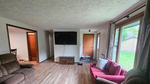 En rummelig stue med et stort fladskærms-tv, en rød sofa og en brun hjørnesofa.
