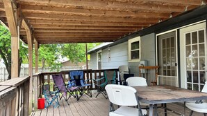 En overdækket terrasse med bord og stole, en træterrasse og et hus i baggrunden.