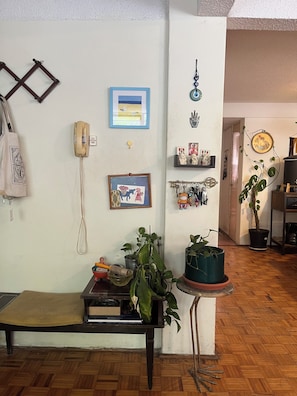 A room with a wooden floor, a bench, a table with a plant, a wall-mounted phone, framed pictures, and a shelf with decorative items. - Authentic urban jungle in Coyoacán, quiet and well-connected neighborhood (Ciudad de México)