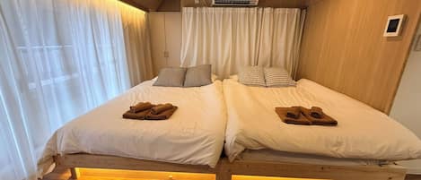 A double bed with white linens and checkered pillows, a wooden headboard, and a bedside table with a lamp.