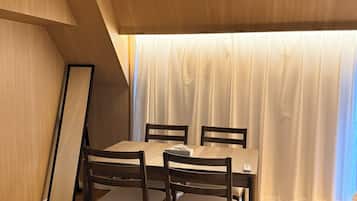 A dining area with a wooden table and chairs, a ceiling with recessed lighting, and a view through a window with curtains.