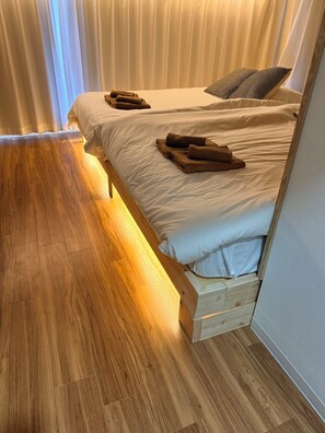 Ein Doppelbett mit weißer Bettwäsche und braunen Handtüchern, Holzboden und ein Fenster mit Vorhängen.
