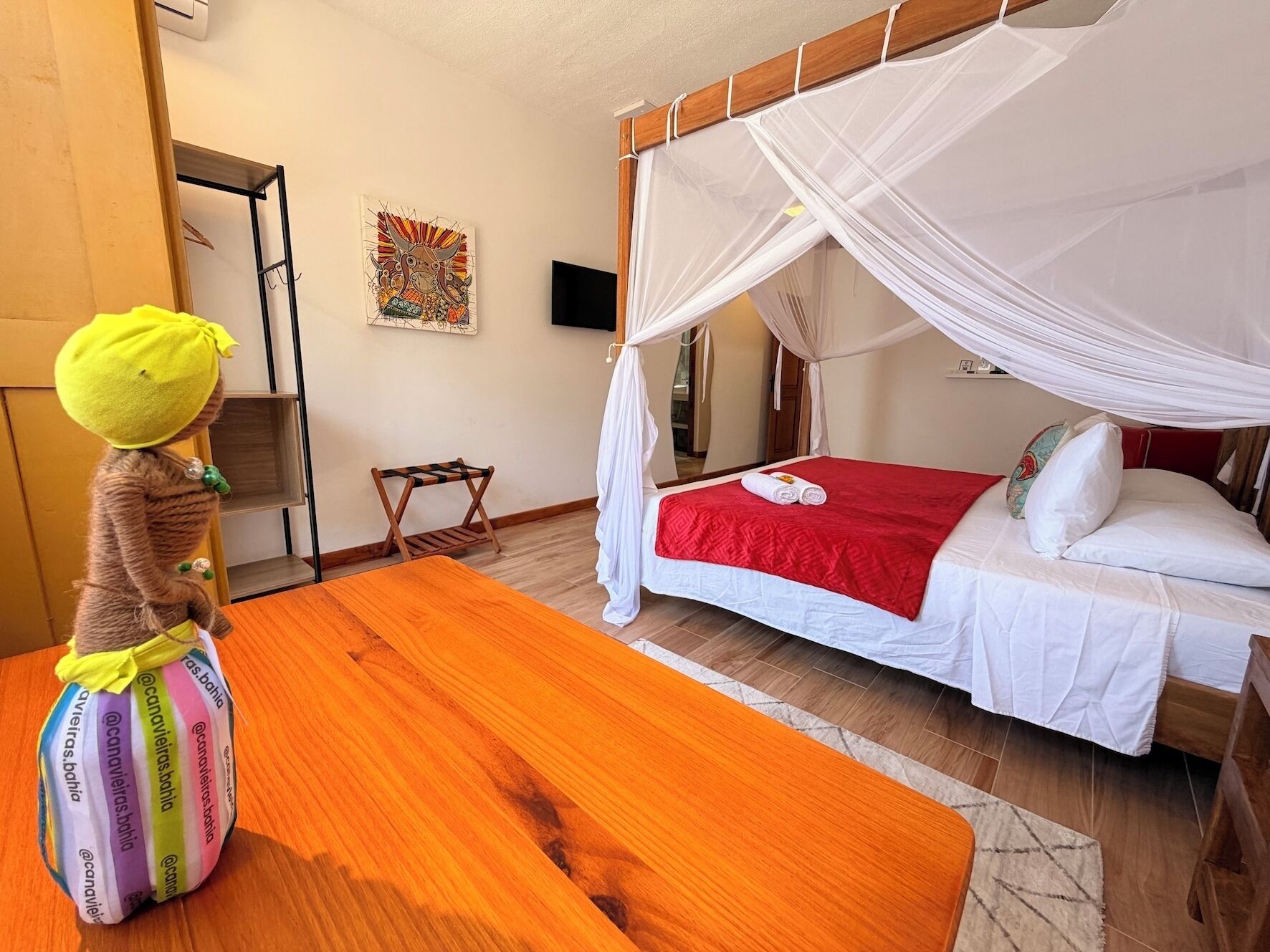 A room with a bed under a white canopy, a wooden table, and a small bench.
