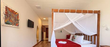 A bedroom with a four-poster bed, a wooden floor, a wall-mounted TV, and a colorful artwork.